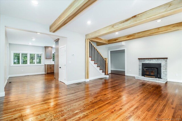 unfurnished living room featuring beamed ceiling, a fireplace, and hardwood / wood-style flooring