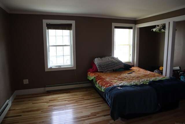 bedroom featuring light hardwood / wood-style floors, baseboard heating, ornamental molding, and multiple windows