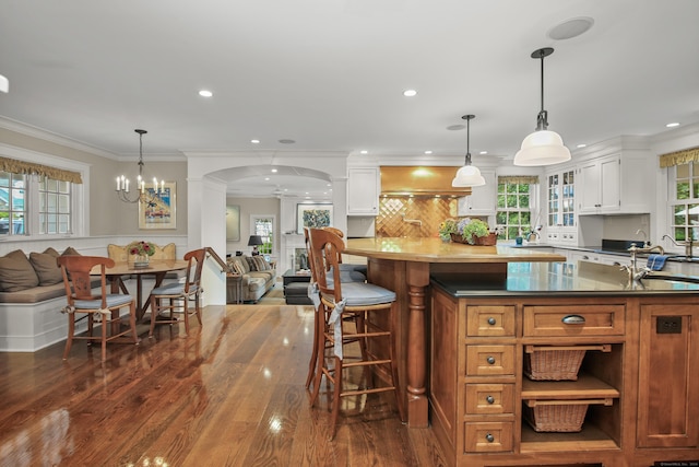 kitchen with arched walkways, glass insert cabinets, hanging light fixtures, white cabinetry, and a sink