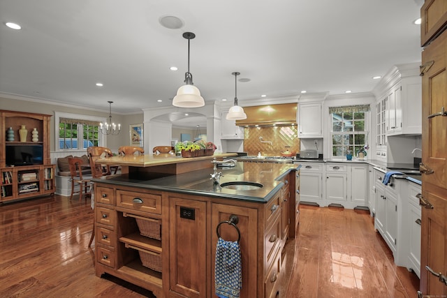 kitchen featuring dark countertops, a kitchen island with sink, white cabinetry, and hanging light fixtures