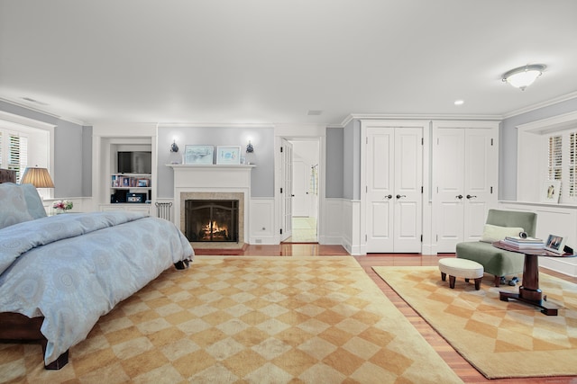 bedroom with a warm lit fireplace, a decorative wall, a wainscoted wall, ornamental molding, and two closets