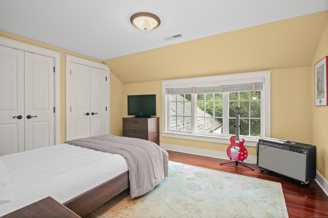 bedroom with dark wood-style floors, two closets, visible vents, vaulted ceiling, and baseboards