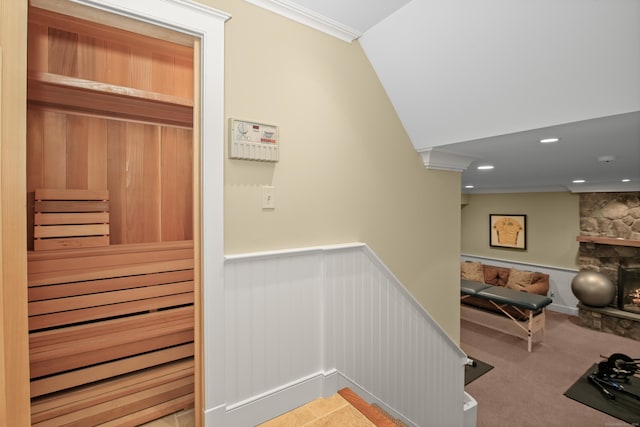 stairway with a stone fireplace, a sauna, wainscoting, and crown molding