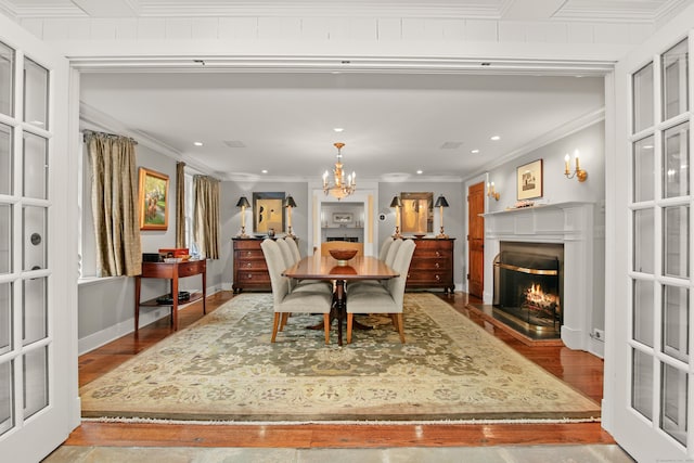 dining space with a chandelier, baseboards, a lit fireplace, light wood finished floors, and crown molding