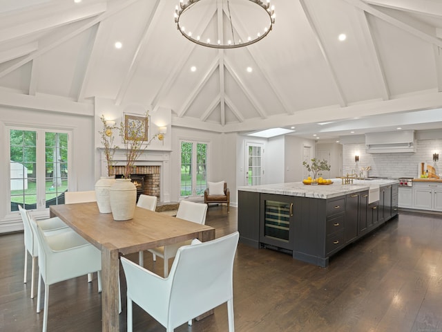 dining area featuring beamed ceiling, high vaulted ceiling, wine cooler, and a brick fireplace