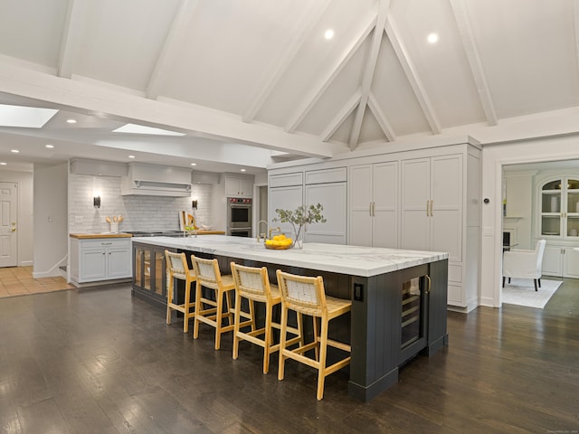 kitchen featuring a large island, light stone countertops, tasteful backsplash, a kitchen bar, and vaulted ceiling with skylight