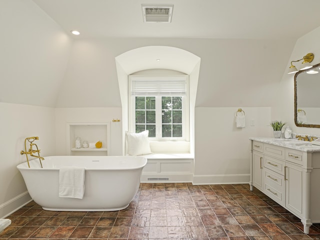 bathroom featuring vanity, a bath, and vaulted ceiling