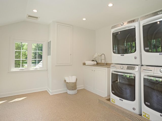 laundry room featuring cabinets, stacked washer and dryer, and sink