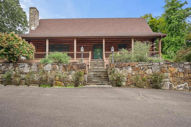 cabin featuring a shingled roof, log exterior, a chimney, stairs, and a porch