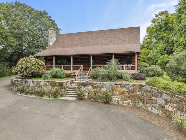 cabin featuring roof with shingles, a chimney, a porch, stairway, and log exterior