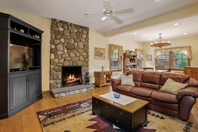 living room featuring light wood-type flooring, ceiling fan with notable chandelier, a fireplace, and beam ceiling