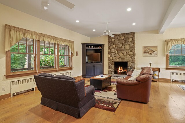 living room featuring ceiling fan, radiator, a stone fireplace, and light hardwood / wood-style floors