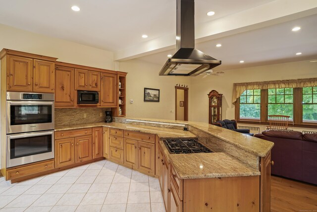 kitchen featuring beamed ceiling, appliances with stainless steel finishes, island range hood, kitchen peninsula, and light stone counters