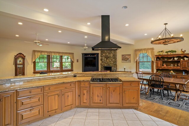 kitchen featuring ceiling fan with notable chandelier, island range hood, light hardwood / wood-style flooring, and light stone counters