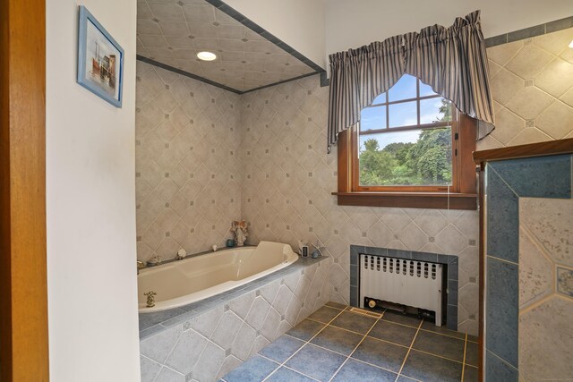 bathroom featuring tile patterned flooring, tile walls, tiled tub, and radiator