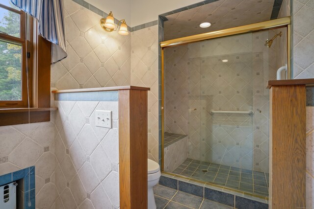 bathroom featuring tile walls, toilet, a healthy amount of sunlight, and a shower with shower door