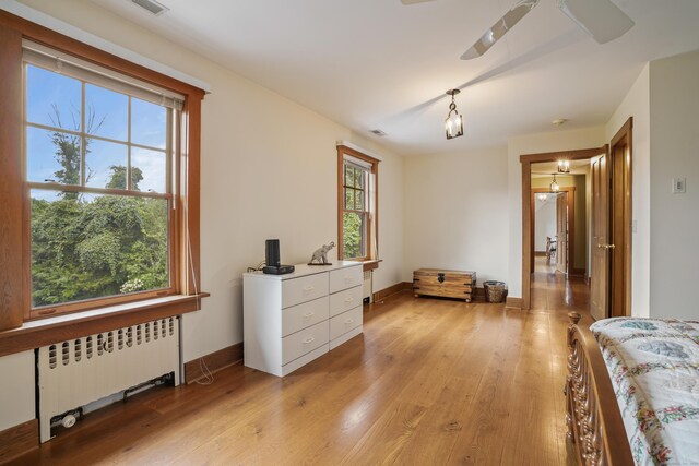 bedroom with multiple windows, light hardwood / wood-style floors, and radiator heating unit