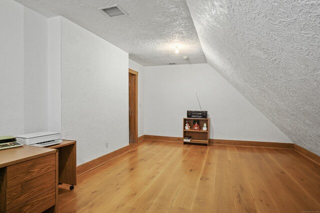 additional living space featuring a textured ceiling, vaulted ceiling, and light hardwood / wood-style floors