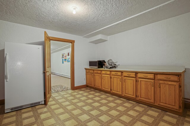 kitchen with white refrigerator, a textured ceiling, and baseboard heating