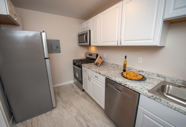 kitchen with white cabinetry, light stone counters, stainless steel appliances, and sink