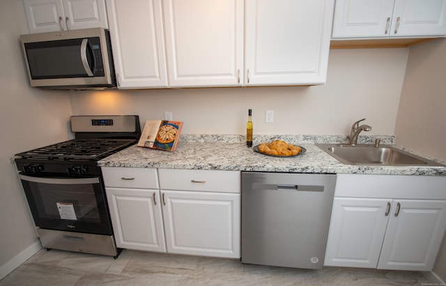 kitchen with appliances with stainless steel finishes, light stone countertops, sink, and white cabinets