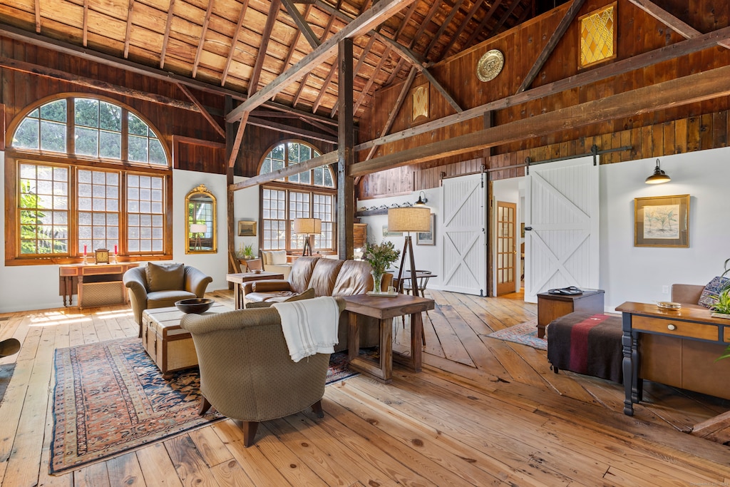 living room with high vaulted ceiling, light hardwood / wood-style flooring, wood walls, a barn door, and wood ceiling