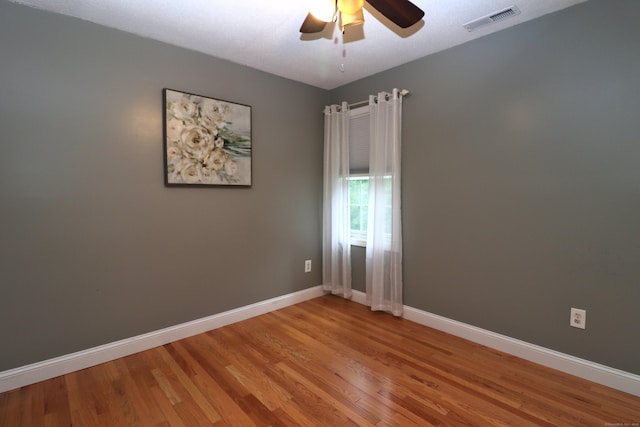 empty room featuring a ceiling fan, wood finished floors, visible vents, and baseboards