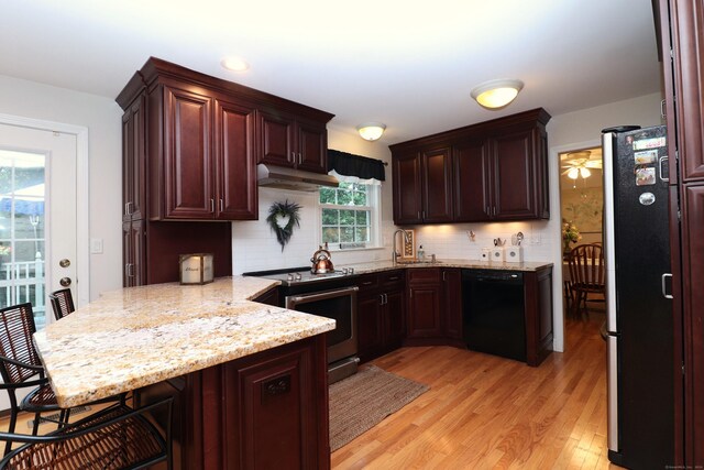 kitchen with decorative backsplash, a kitchen breakfast bar, light hardwood / wood-style flooring, light stone counters, and stainless steel appliances