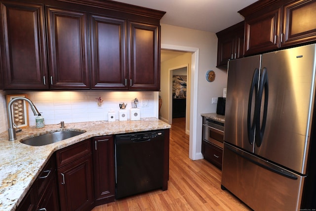 kitchen featuring black dishwasher, light wood finished floors, tasteful backsplash, freestanding refrigerator, and a sink