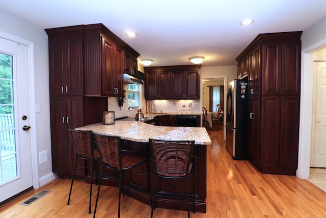 kitchen with visible vents, freestanding refrigerator, light wood-type flooring, a peninsula, and a kitchen breakfast bar