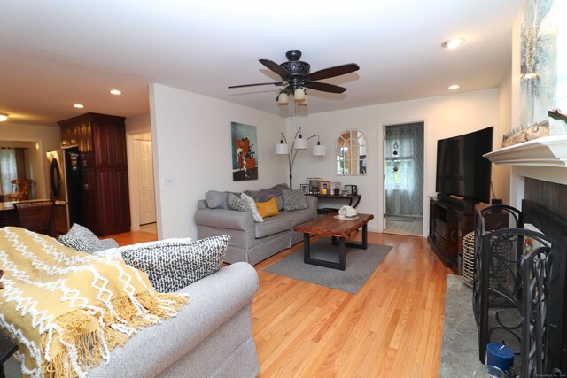 living room with ceiling fan, a tiled fireplace, and hardwood / wood-style floors