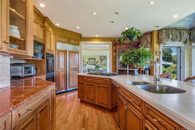 kitchen with decorative backsplash, sink, built in appliances, and light hardwood / wood-style flooring