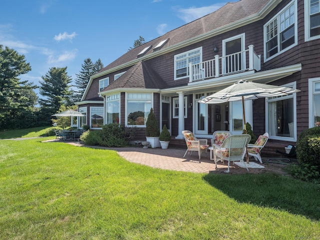 back of house with a balcony, a patio area, and a lawn