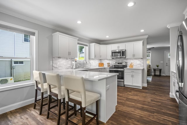 kitchen featuring white cabinetry, sink, kitchen peninsula, a breakfast bar area, and appliances with stainless steel finishes