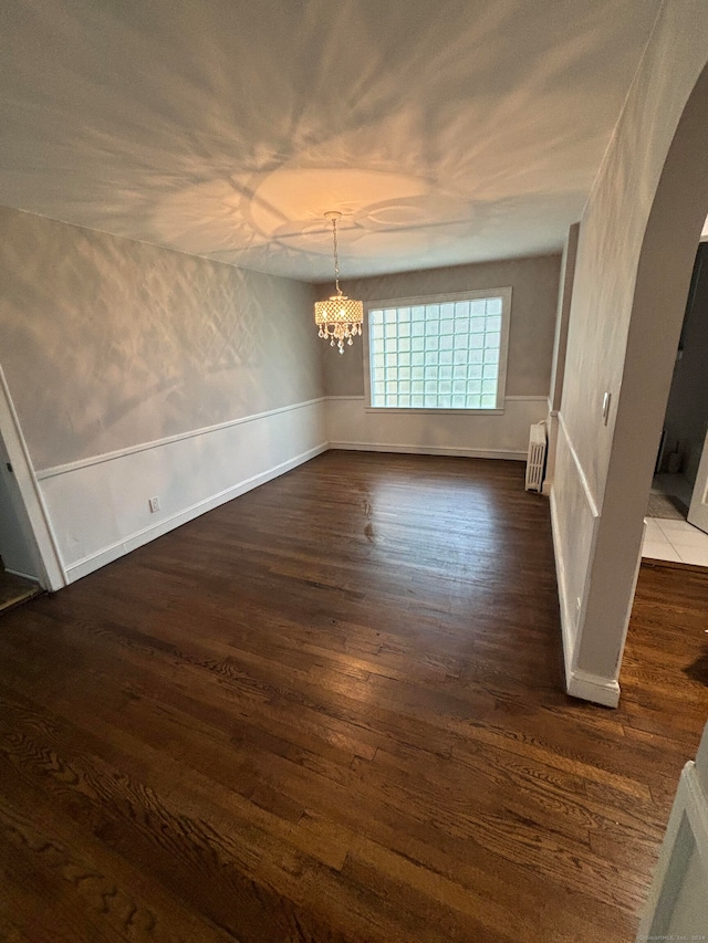 empty room with radiator heating unit, dark hardwood / wood-style flooring, and an inviting chandelier