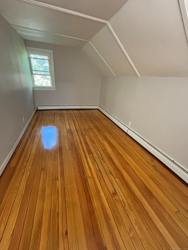 additional living space featuring light wood-type flooring, baseboard heating, and vaulted ceiling