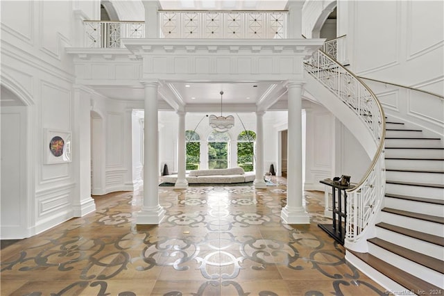 entrance foyer featuring an inviting chandelier, crown molding, a high ceiling, and decorative columns