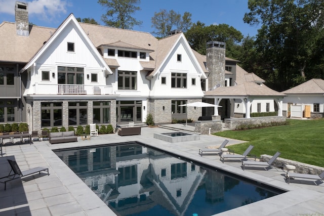 back of house featuring a balcony, a patio, a swimming pool with hot tub, and a yard