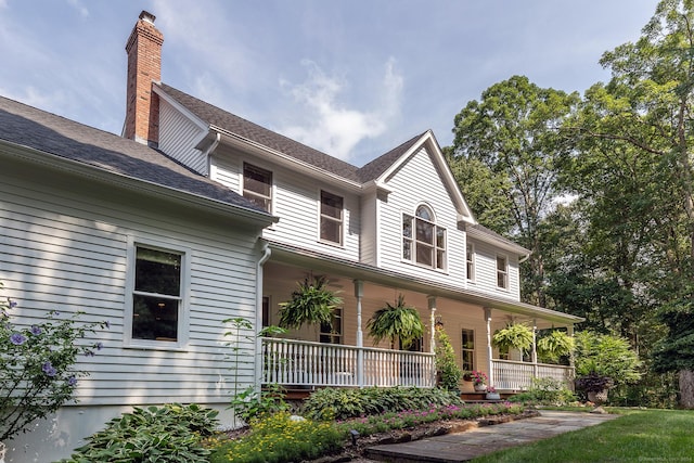 farmhouse-style home with a porch, a shingled roof, and a chimney