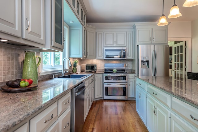 kitchen featuring pendant lighting, stainless steel appliances, tasteful backsplash, a sink, and wood finished floors