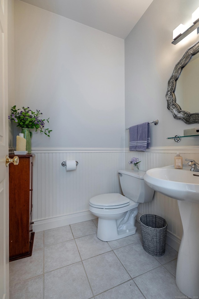 bathroom featuring toilet, a wainscoted wall, a sink, and tile patterned floors