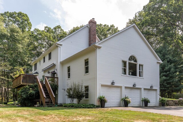 view of side of home featuring a chimney, a lawn, stairway, an attached garage, and a deck