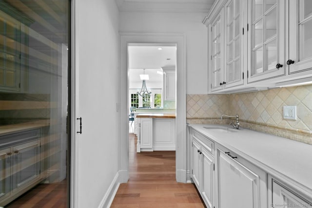 bar with light wood-type flooring, crown molding, backsplash, white cabinetry, and sink