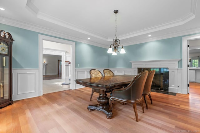 dining room featuring an inviting chandelier, a raised ceiling, ornamental molding, and light hardwood / wood-style floors