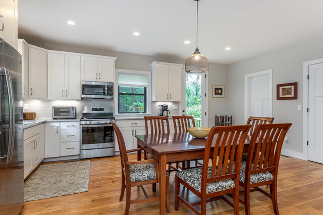 kitchen with light wood-type flooring, white cabinetry, appliances with stainless steel finishes, and hanging light fixtures