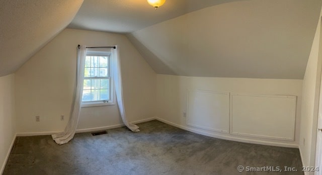 additional living space with dark carpet and vaulted ceiling