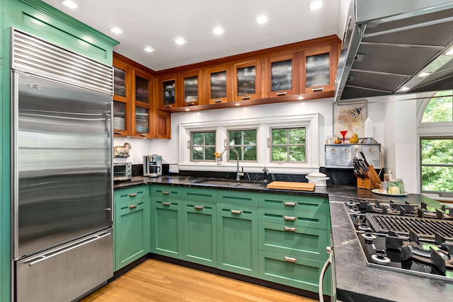 kitchen featuring exhaust hood, built in refrigerator, a sink, green cabinetry, and black gas stovetop