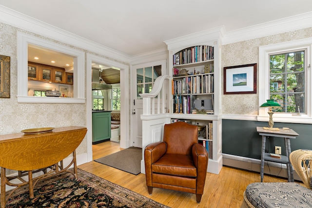 living area with crown molding, a baseboard heating unit, light wood-style flooring, and wallpapered walls