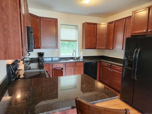 kitchen with black appliances, sink, dark stone counters, and light hardwood / wood-style floors