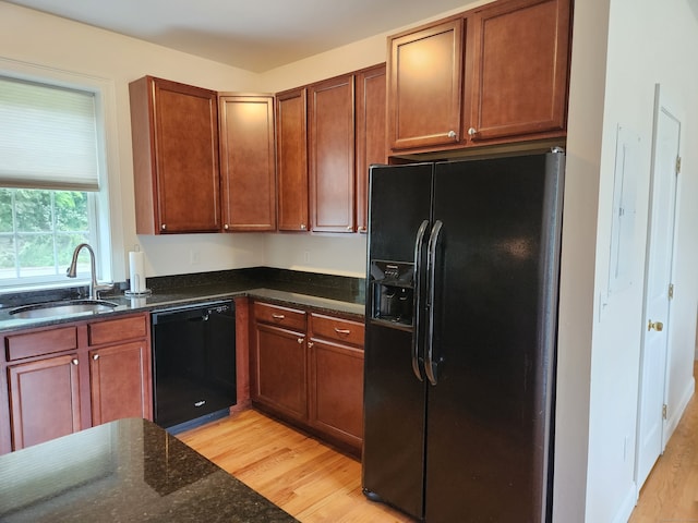 kitchen with black appliances, sink, light hardwood / wood-style flooring, and dark stone counters